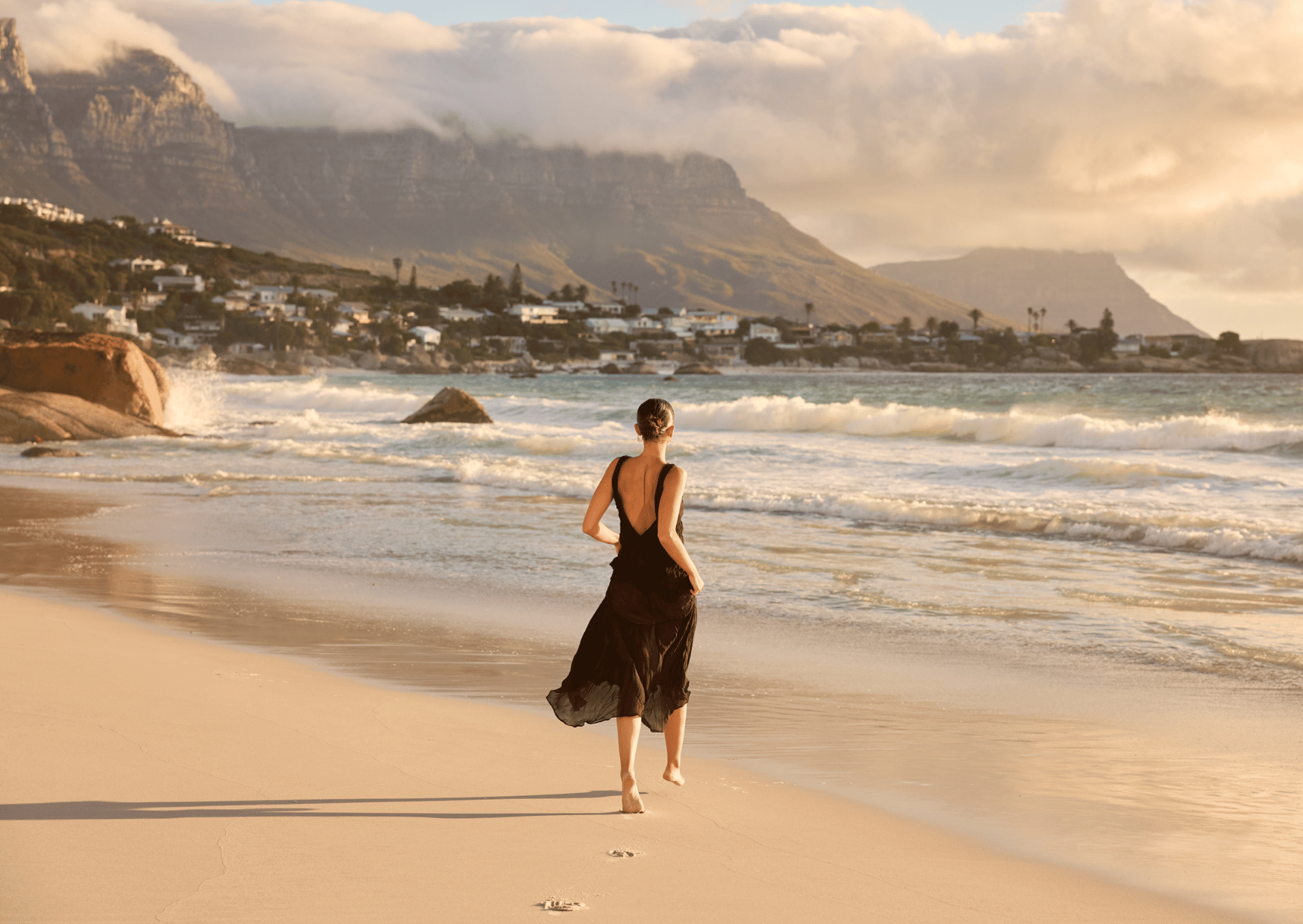 Woman in a black dress standing on a beach with Table Mountain in the background